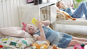 a funny kid girl with a toy phone in bed repeats after older sister.