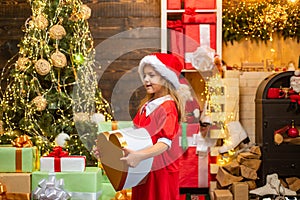 Funny kid holding Christmas gift. Child with gift. Models child having fun with gift. Kid having fun near Christmas tree