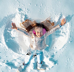 Funny kid making snow angel. Child girl playing and making a snow angel in the snow. Top view.