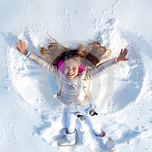 Funny kid making snow angel. Child girl playing and making a snow angel in the snow. Top view.