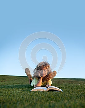 Funny kid reading the book in spring park. Child boy with a book in the garden. Kid is readding a book playing outdoors