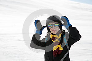 Funny kid with in warm clothes and protection equipment taunts. White snow background.