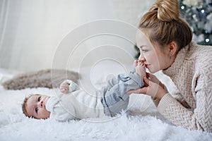 Funny kid on a white bed with his mother near the Christmas tree