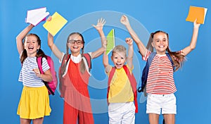 Funny kids with backpacks behind happily jumping raising their hands up with exercise books