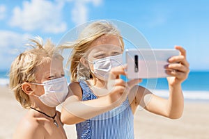 Funny kids in face masks taking selfie photo on beach