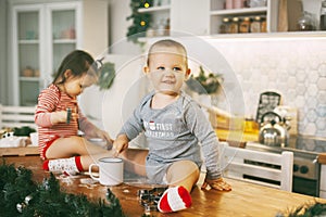 Funny kids sit on the kitchen table and play with cookie cutters. Children help bake cookies for Christmas and New year