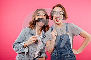 Funny ladies friends holding fake moustache and glasses.