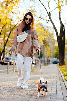 Funny lady in casual clothes walks a dog breed biewer terrier on a leash on an autumn street on a background of trees with yellow