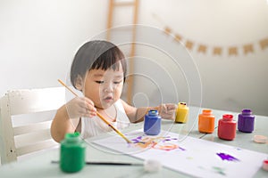 Funny laughing asian baby girl drawing with colorful pencils at