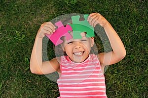 Funny laughing autistic girl playing with colored puzzle pieces lying on grass