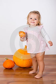 Funny laughing baby girl playing with a huge pumpkin