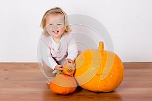 Funny laughing baby girl playing with a huge pumpkin