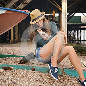 Funny laughing young woman with long legs looking on her gumshoes under the old pier. photo