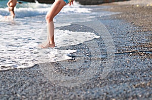 Funny legs of a girl and boy on the beach run away and jump into the sea waves at sunset