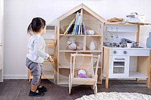 Funny little Asian girl playing in her room. A cute toddler in casual clothes looks at toys and books. A child in kindergarten