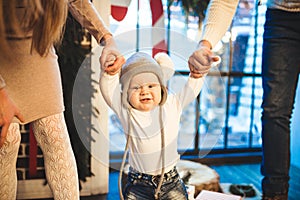 Funny little baby boy 1 year old learning walk home in winter in a decorated New Year house. Young family dad and mom hold by the
