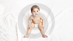 Funny little baby in a diaper. Portrait of a cute baby 9 months old sitting on a white blanket