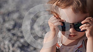 Funny little baby girl wears big sunglasses on the beach