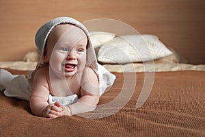 Funny little baby lies on bed wrapped in white towel with hood