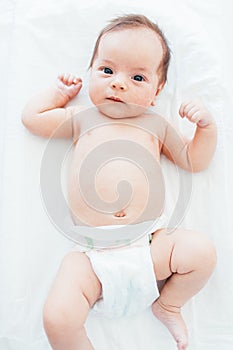 Funny little baby wearing a diaper lying on a white sheet. Child after bath or shower. Infant nappy change and skin care