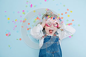 Funny little birthday girl lies on a floor with a confetti pieces