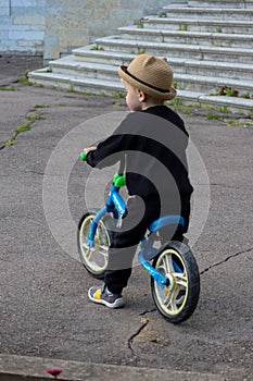 funny little blond child in a hat riding a blue bike