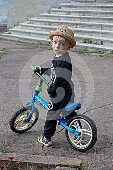 funny little blond child in a hat riding a blue bike