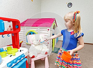 Funny little blond girl feeding her friend teddy bear