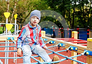 Funny little boy clime in the rope web on playground. Cute boy play and climb outdoors on sunny summer day