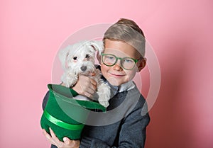 Funny little boy with green hat with little white dog on St. Patrick's Day celebration party. Kid in green glasses