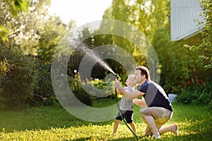 Funny little boy with his father playing with garden hose in sunny backyard