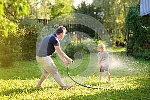 Funny little boy with his father playing with garden hose in sunny backyard. Preschooler child having fun with spray of water