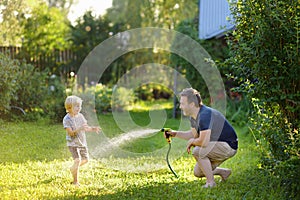 Funny little boy with his father playing with garden hose in sunny backyard. Preschooler child having fun with spray of water