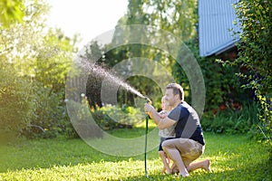 Funny little boy with his father playing with garden hose in sunny backyard. Preschooler child having fun with spray of water