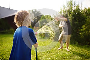 Funny little boy with his father playing with garden hose in sunny backyard. Preschooler child having fun with spray of water.