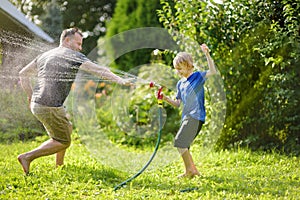 Funny little boy with his father playing with garden hose in sunny backyard. Preschooler child having fun with spray of water.