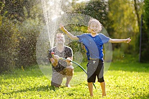 Funny little boy with his father playing with garden hose in sunny backyard. Preschooler child having fun with spray of water.