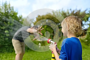 Funny little boy with his father playing with garden hose in sunny backyard. Preschooler child having fun with spray of water.