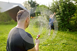 Funny little boy with his father playing with garden hose in sunny backyard. Preschooler child having fun with spray of water.