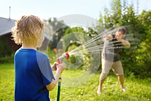 Funny little boy with his father playing with garden hose in sunny backyard. Preschooler child having fun with spray of water.