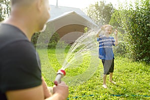 Funny little boy with his father playing with garden hose in sunny backyard. Preschooler child having fun with spray of water.