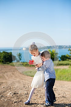 Funny little boy hugging girl holding bouquet of flowers on sea background in spring