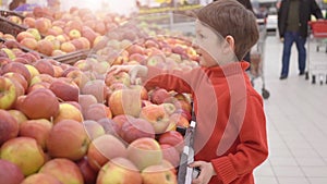 Funny little boy picking apple from the box, during family shopping in hypermarket