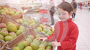 Funny little boy picking mango from the box, during family shopping in hypermarket