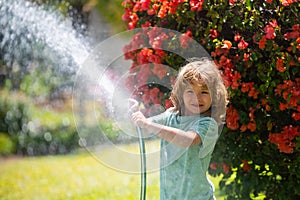 Funny little boy playing with garden hose in backyard. Child having fun with spray of water on yard nature background