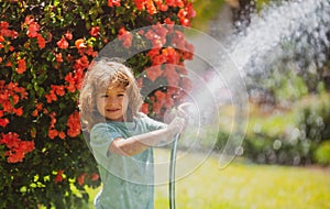 Funny little boy playing with garden hose in backyard. Child having fun with spray of water on yard nature background