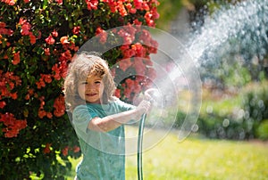 Funny little boy playing with garden hose in backyard. Child having fun with spray of water on yard nature background