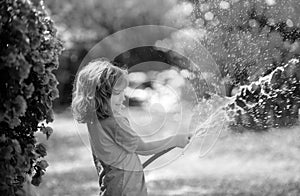 Funny little boy playing with garden hose in backyard. Child having fun with spray of water on yard nature background