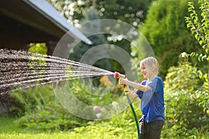 Funny little boy playing with garden hose in sunny backyard. Preschooler child having fun with spray of water. Summer vacation in
