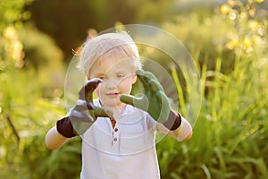 Funny little boy wearing garden gloves. Garden tools and gloves outdoors.